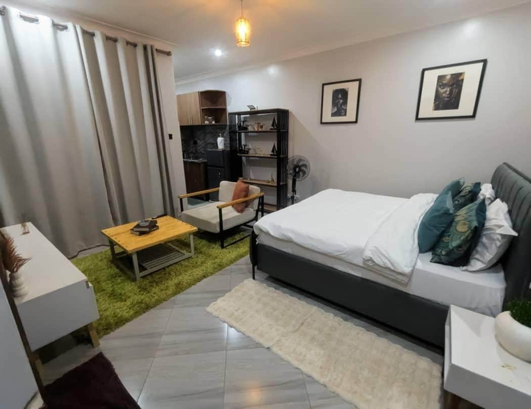 A modern bedroom with a bed, a small table, a chair, a bookshelf, and a fan.