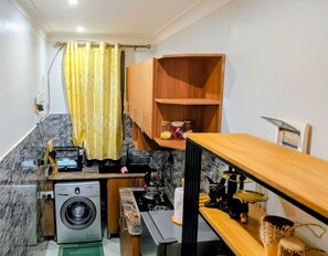 A compact kitchen with a washing machine, a small dining area, and a wooden shelf unit. - Luxury studio kyanja ring road (Kampala)