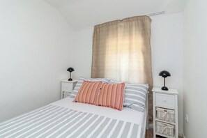 Uma cama com roupa de cama listrada, um travesseiro listrado vermelho e branco e duas mesas de cabeceira com abajures.