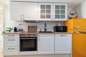 A kitchen with white cabinets, a black oven, a microwave, and a yellow refrigerator. - Traditional stone house with terrace, near the beach (Trogir)
