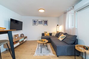 A modern living room with a flat-screen TV, a sofa, a coffee table, and a dining area with a chair and a small table. - Traditional stone house with terrace, near the beach (Trogir)