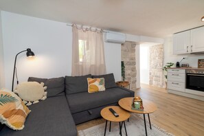 A modern living room with a grey sofa, a small round table, a remote control, and a wall-mounted air conditioner. - Traditional stone house with terrace, near the beach (Trogir)