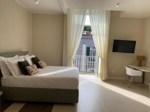Habitación de hotel con cama, televisor, una mesita y vistas al balcón.