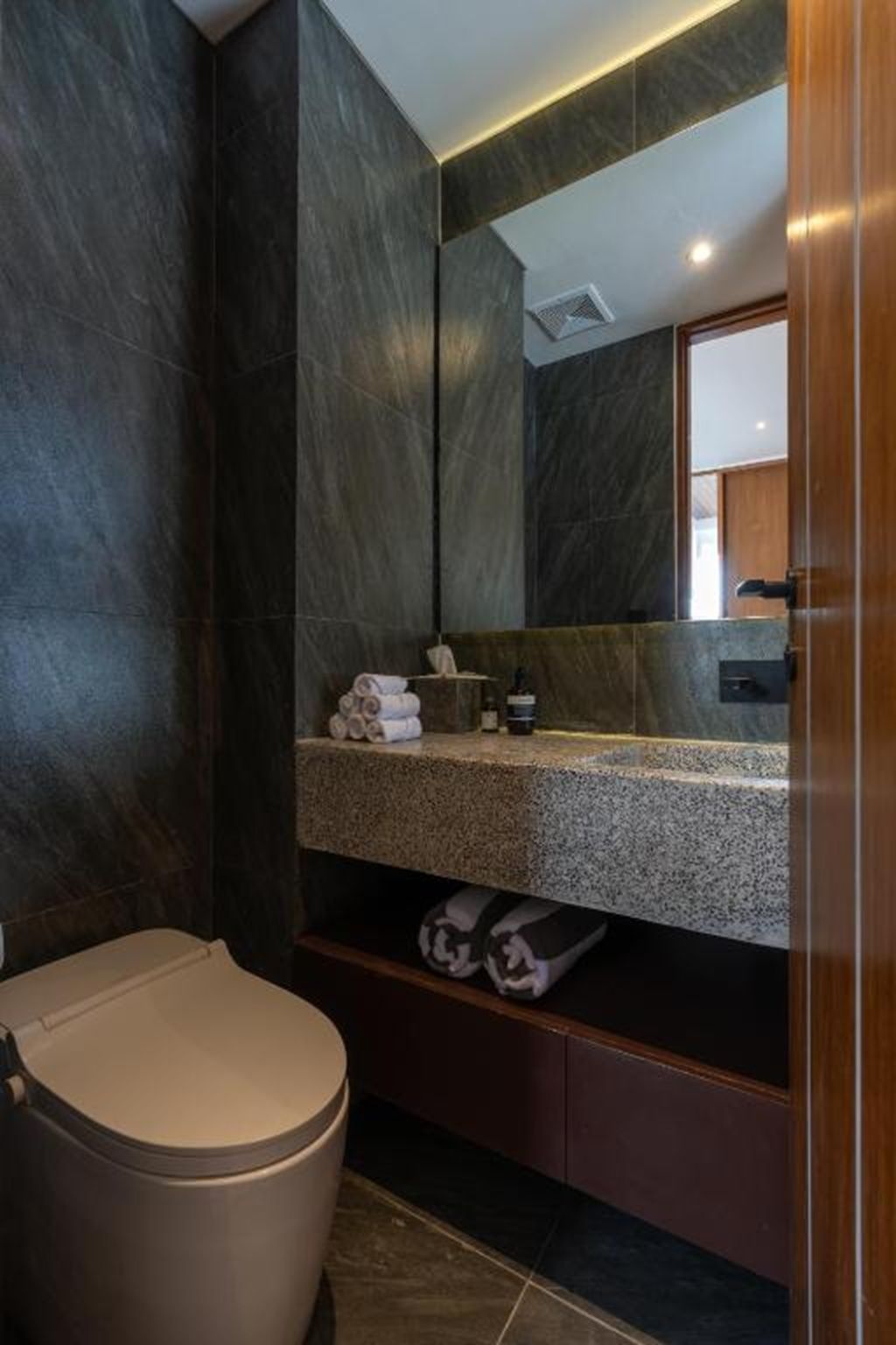 A modern bathroom with a dark marble wall, a granite countertop, a toilet, and a mirror.