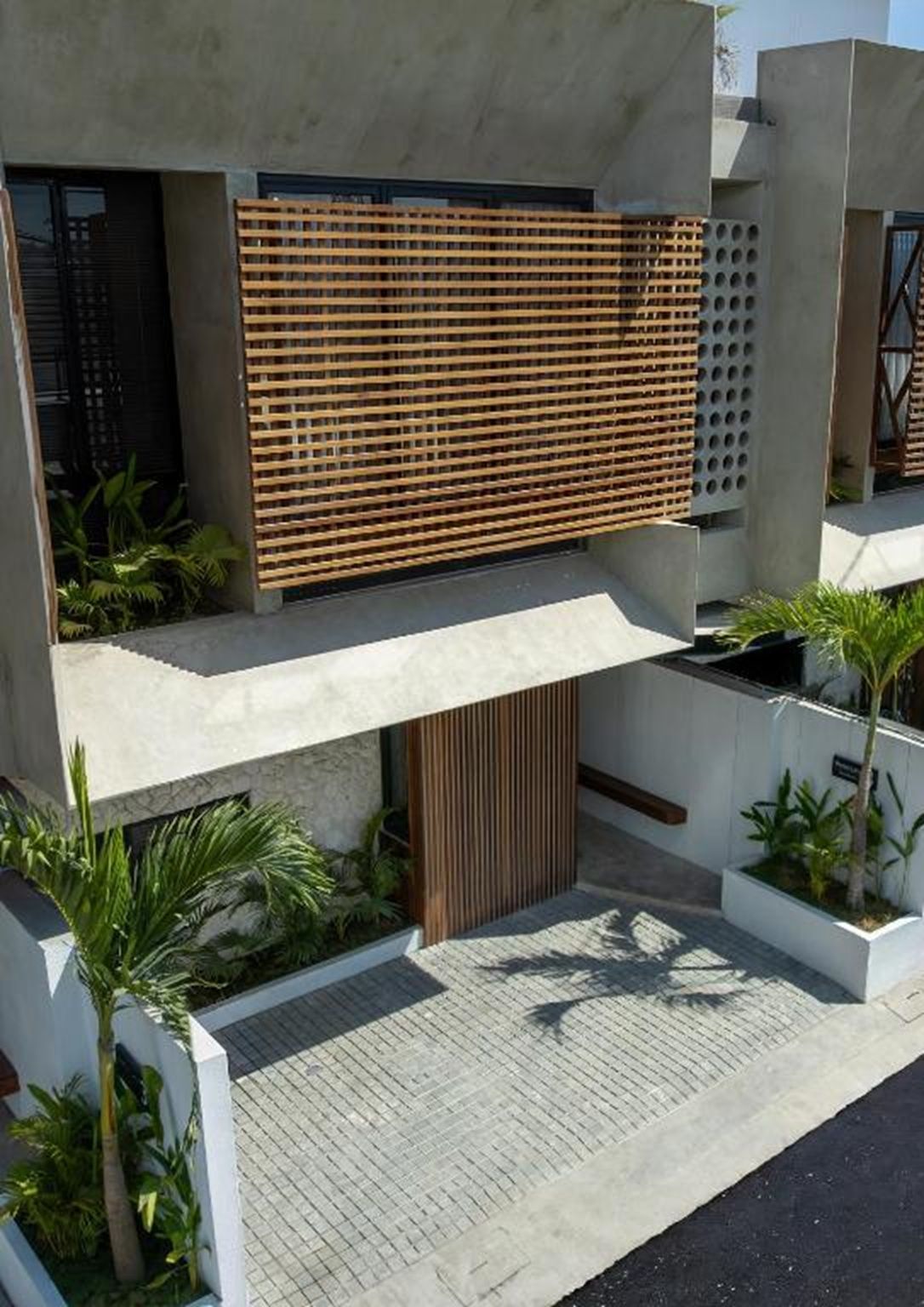 A modern building with a flat roof, a wooden slatted facade, and a paved courtyard with potted plants.