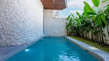 A swimming pool with stone walls, surrounded by lush greenery.