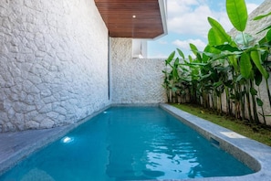 Una piscina con paredes de piedra, rodeada de exuberante vegetación.