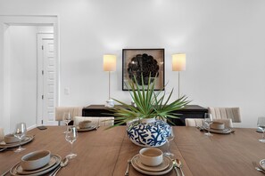 A dining room with a wooden table set for a meal, a decorative vase, and a framed artwork on the wall. - SeaLuxe Brand New Construction, Beach Front, Elevated Pool, Hot Tub,  Sleeps 14 (St. George Island)