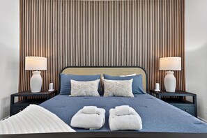 A hotel room with a bed, two bedside tables, lamps, and a large window. - SeaLuxe Brand New Construction, Beach Front, Elevated Pool, Hot Tub,  Sleeps 14 (St. George Island)