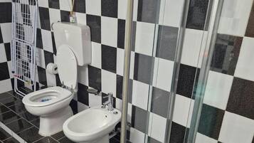 A bathroom with a checkered black and white tile wall, a toilet, a bidet, and a glass-enclosed shower area.