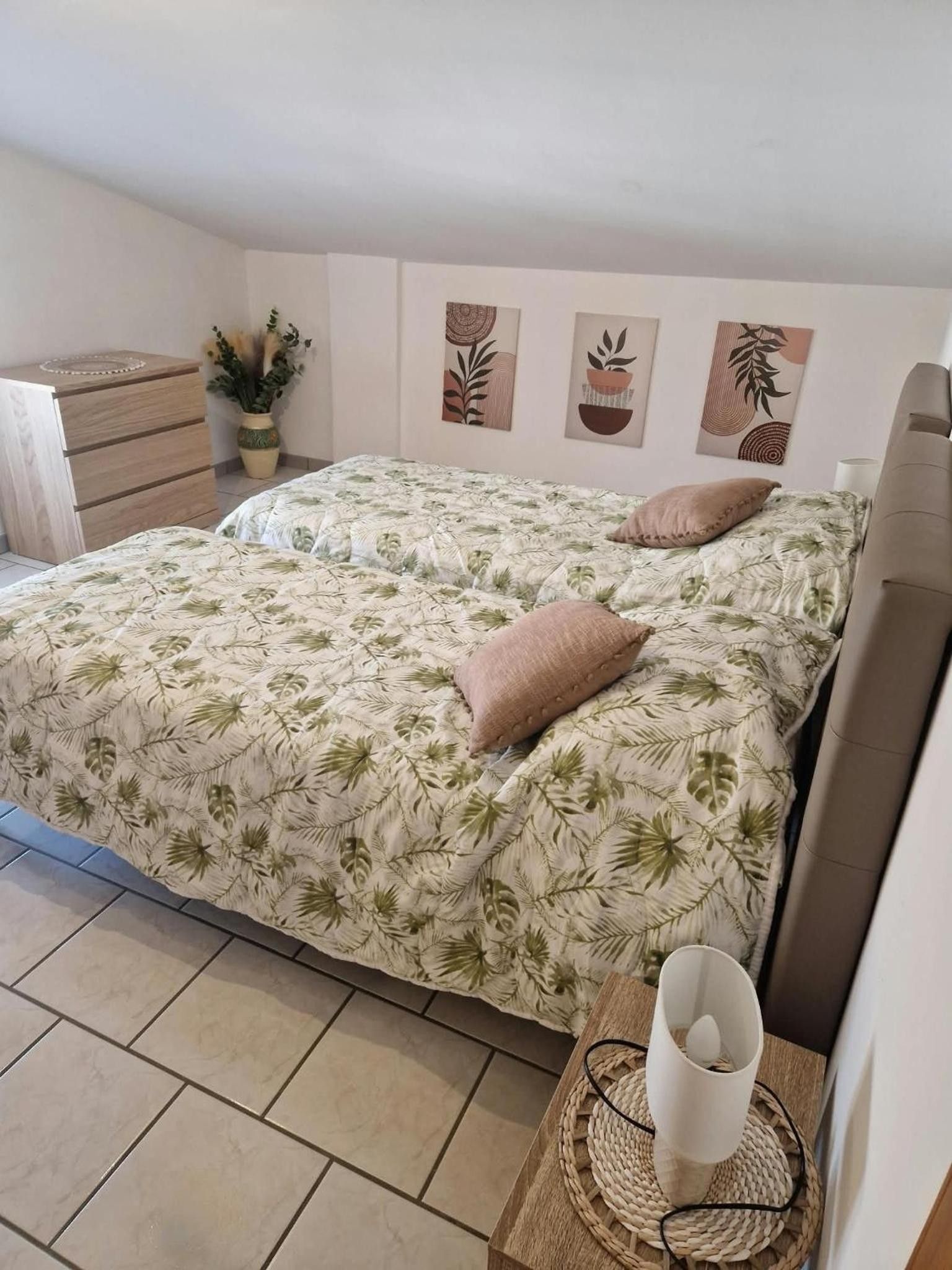 A bedroom with a bed, a bedside table, a chair, and a wall with three artworks.