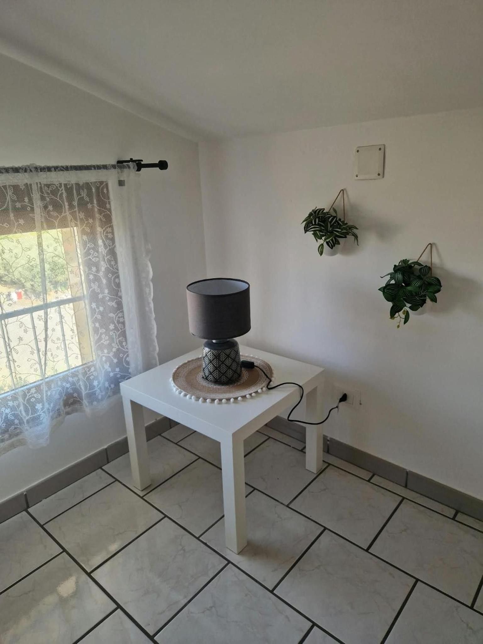 A room with a white table, a lamp, and two potted plants on the wall.
