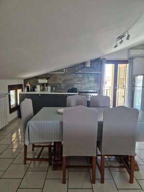 A dining area with a table and chairs, a kitchen in the background, and a view through an open door. - Apartment 'Tra Mare E Monti' with Mountain View, Wi-Fi and Air Conditioning (Paglieta)
