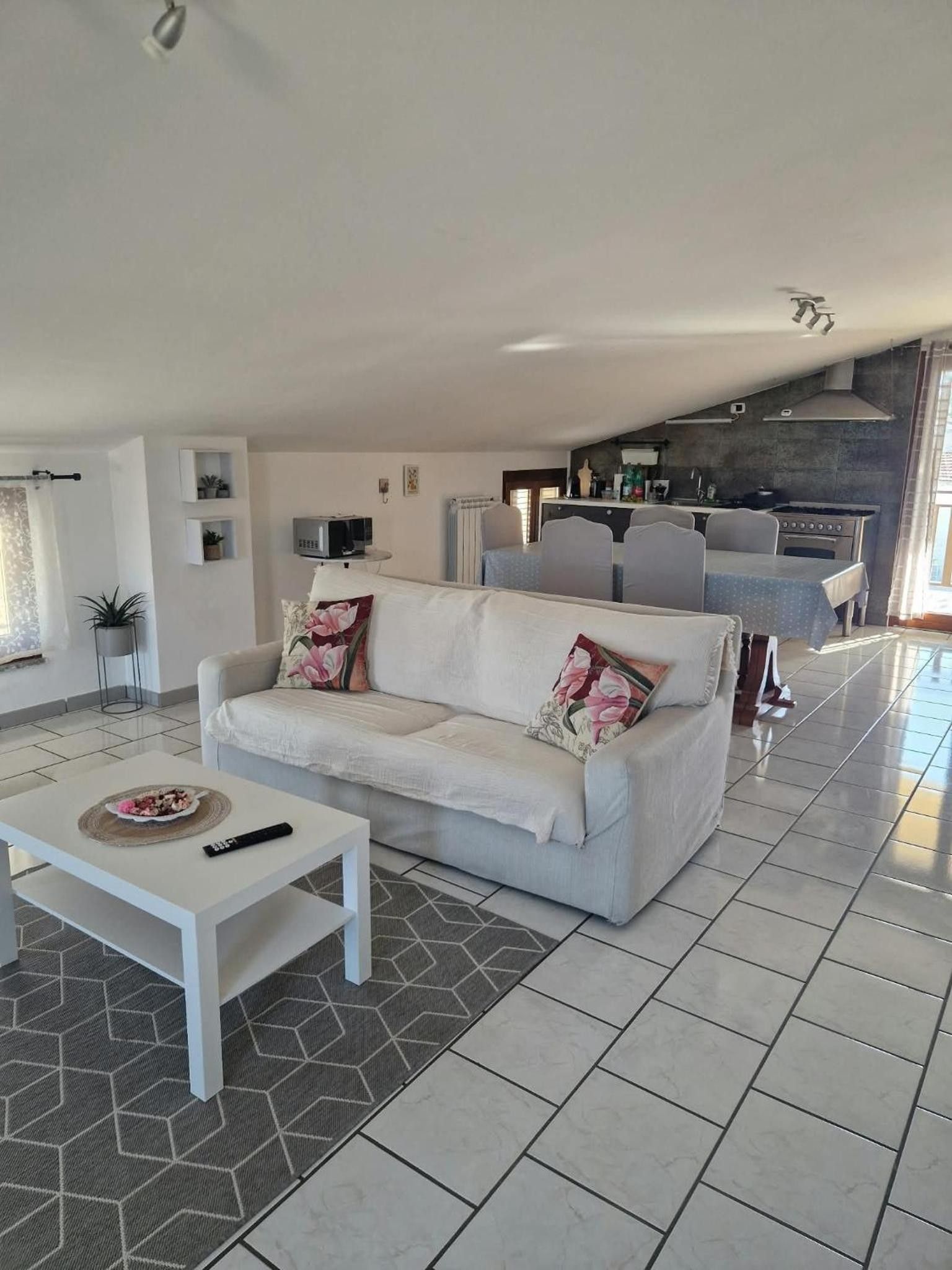 Amplia sala de estar con un sofá blanco, una mesa de centro y una mesa de comedor preparada para cuatro comensales.