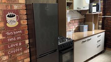Una cocina con pared de ladrillo, un refrigerador de acero inoxidable, una estufa a gas y armarios blancos.