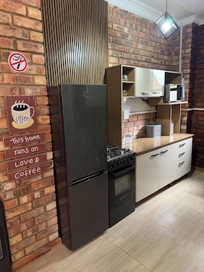 A kitchen with a brick wall, a stainless steel refrigerator, a gas stove, and white cabinetry.