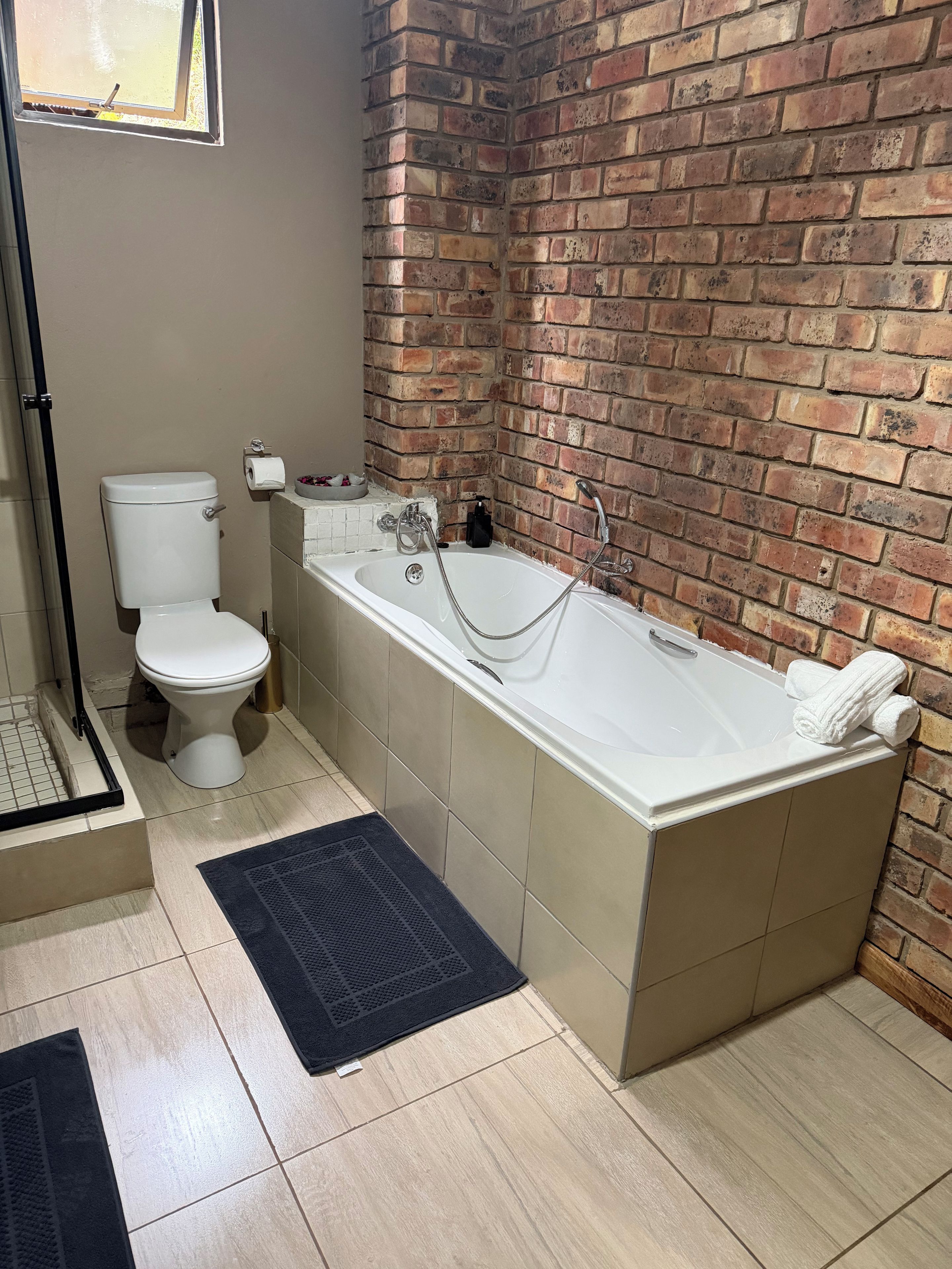 Een badkamer met een witte badkuip, een toilet en een bakstenen muur.