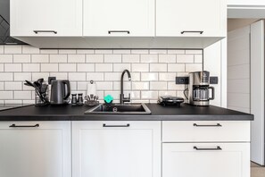 A modern kitchen with white cabinets, a black countertop, a stainless steel sink, and a coffee maker. - Studio Petar with private parking and balcony near the beach (Kaštel Štafilić)