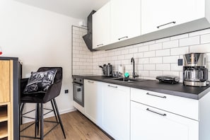 Eine moderne Küche mit weißen Schränken, einer schwarzen Arbeitsplatte, einer Kaffeemaschine und einem schwarzen Stuhl mit Sitzkissen in Stadtansicht.