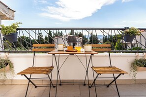 Ein Balkon mit Holztisch und -stühlen, Blumentöpfen und Blick auf die Stadtlandschaft.