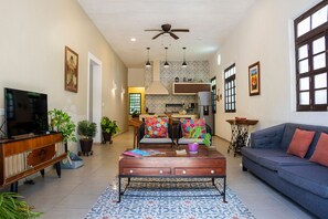 A living room with a television, sofa, coffee table, and a kitchen area in the background. - Casa Grande 5 Blocks to Montejo (Mérida)