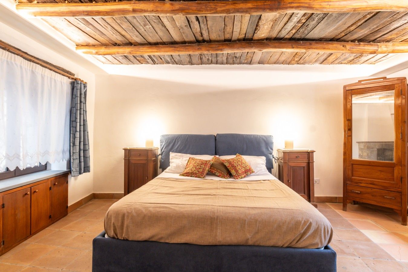 Ein Schlafzimmer mit Holzboden, einem Bett mit zwei Kissen, einem Nachttisch, einem Kleiderschrank und einem Fenster mit Vorhängen.