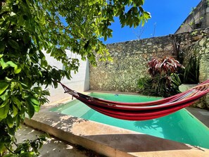 A hammock over a swimming pool with a stone wall and greenery in the background. - Secure Colonial Retreat w Beach Club (Mérida)