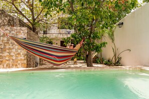 A hammock tied between trees over a swimming pool with a stone wall and a building in the background. - Secure Colonial Retreat w Beach Club (Mérida)