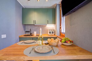 A compact kitchen with a dining table set for two, a bottle of wine, a fruit bowl, and a vintage radio. - Niagara Studio (Sauze d'Oulx)