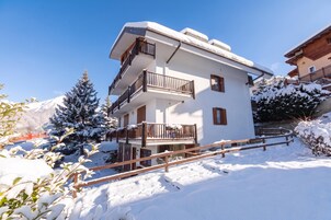 Un edificio a più piani con balconi, circondato da alberi innevati e un cielo sereno.