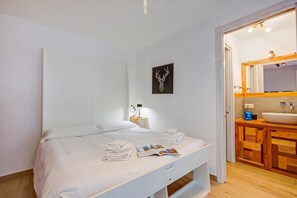 Ein Hotelzimmer mit einem Bett, einem Nachttisch mit Lampe, einem Wandspiegel und einem Badezimmer mit Waschbecken und Holzsärchen.