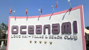 A large sign for Oceanami Long Hai - Villas & Beach Club with multiple flags on top.