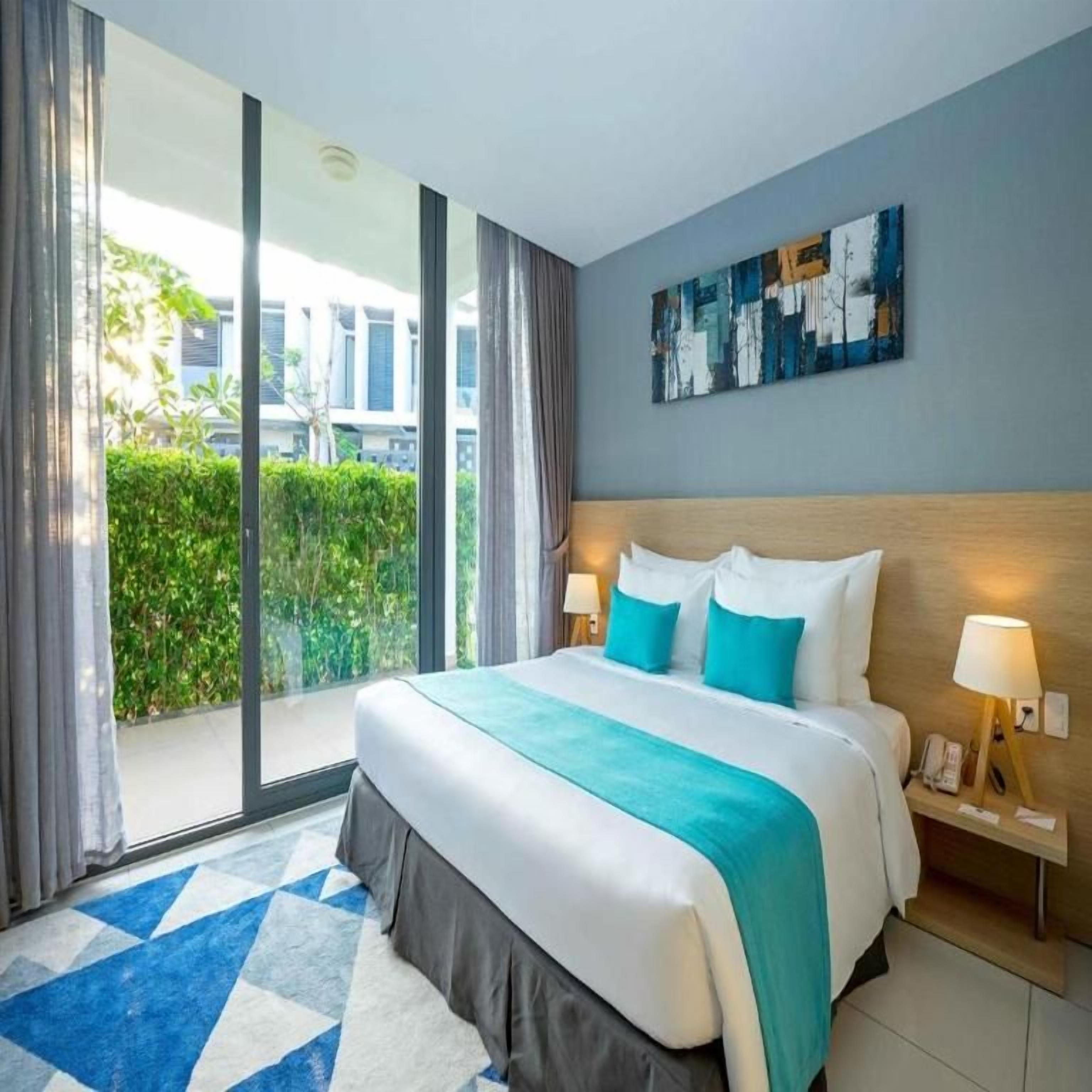 Een hotelkamer met een groot bed, uitzicht op groen en een modern abstract schilderij aan de muur.