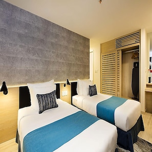 Ein Hotelzimmer mit zwei Betten, einem großen Fenster mit Jalousien, einem Kleiderschrank und einem Spiegel.
