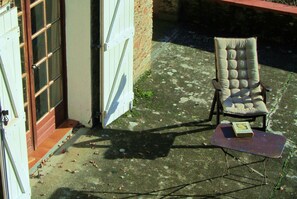 A chair with a cushion and a book on a small table outside a building with a door and windows. - Holiday Home 'Bourdounal' with Swimming River, 2 Hectares of Private Nature, Terrace and Wi-Fi (Crespin)