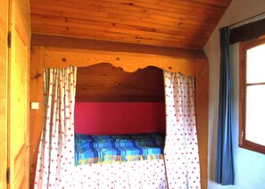 Una habitación con techo de madera, pared roja y ventana con cortinas.