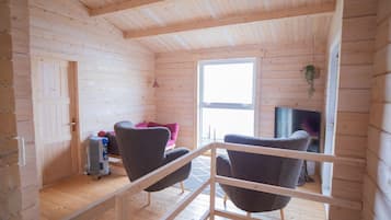 A wooden cabin interior with a high ceiling, a large window, and a TV.
