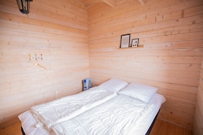 A wooden cabin room with a bed, a heater, and a wall-mounted light fixture. - Geilin 11 (Innan Glyvur)