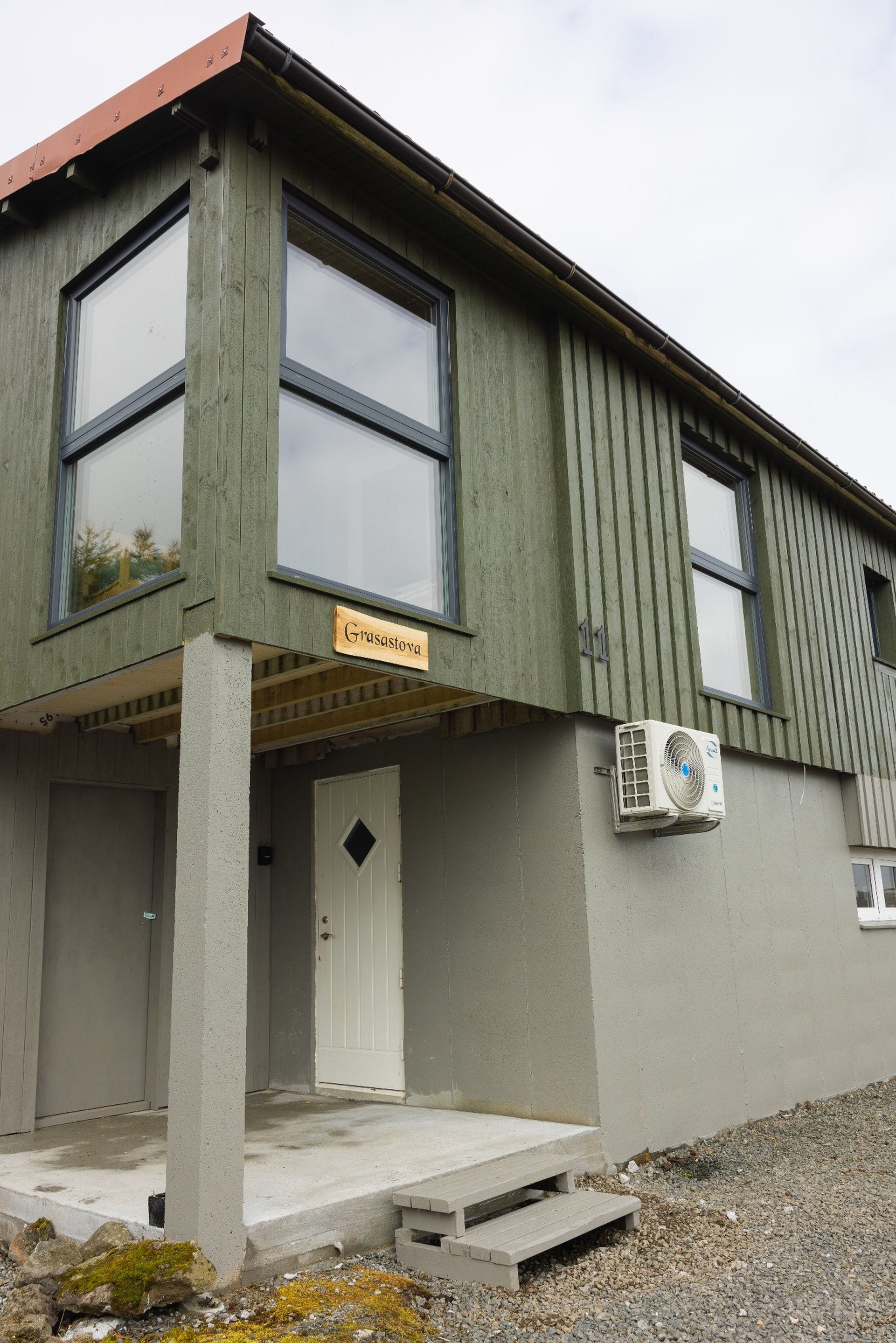 A building with a sign reading 'Grasastova' above the entrance, a door, and an air conditioning unit mounted on the wall.