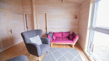 A cozy room with wooden walls, a grey armchair, a pink sofa, and a window.