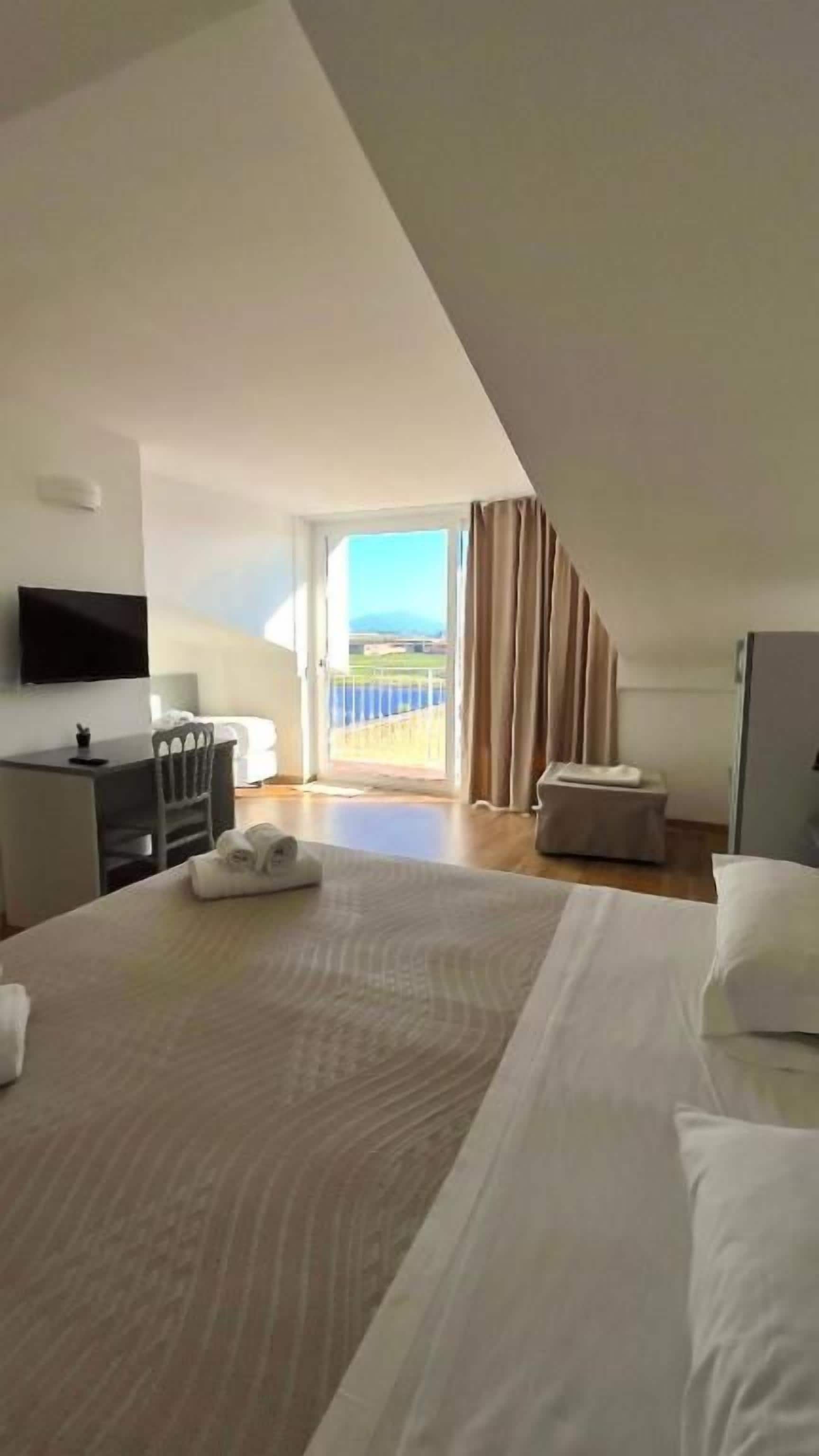 Une chambre d’hôtel avec un lit, un bureau, une chaise, une télévision et un balcon avec des rideaux.