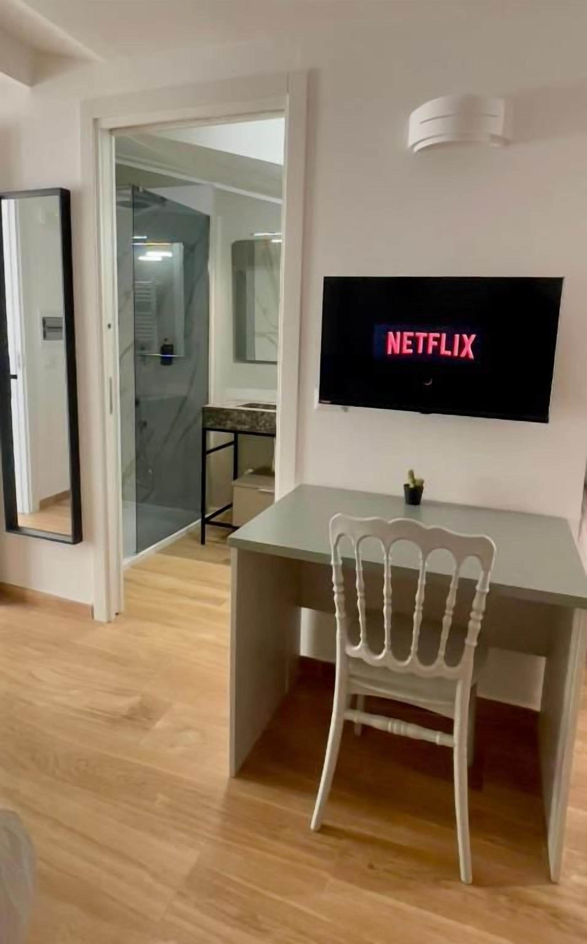 Ett rum med ett skrivbord, en stol, en tv som visar ”NETFLIX” och en dörr som leder till ett annat rum.