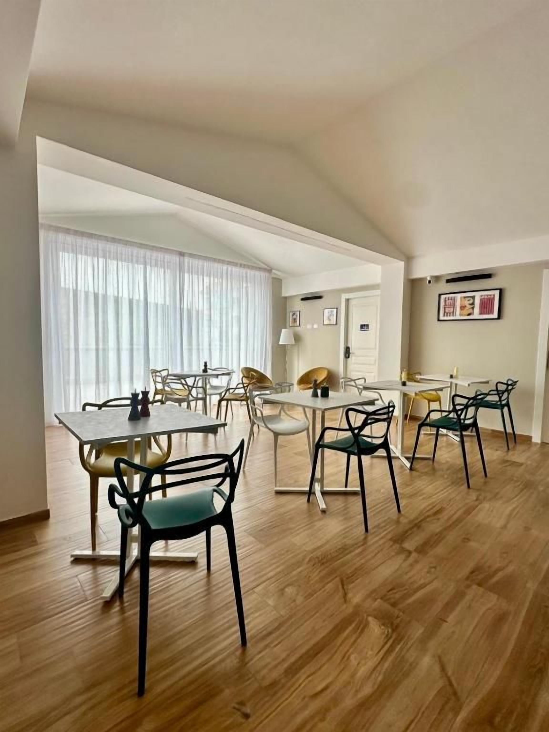 Un espace repas doté d’un plafond haut, d’un plancher en bois et d’un mélange de chaises modernes et classiques.