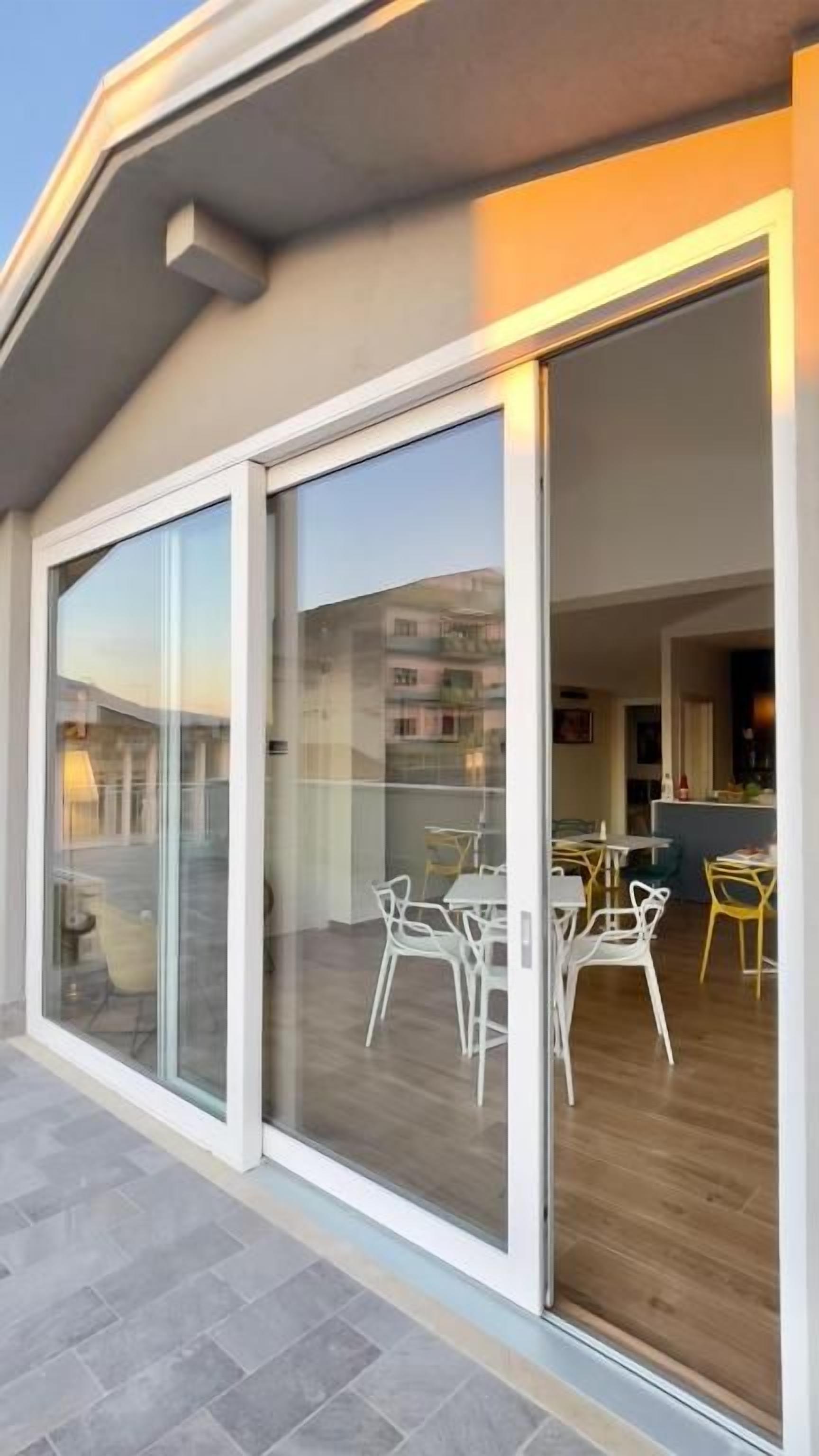 A modern building with large sliding glass doors leading to an outdoor patio area with white chairs and a dining table.