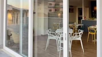 A modern building with large sliding glass doors leading to an outdoor patio area with white chairs and a dining table.