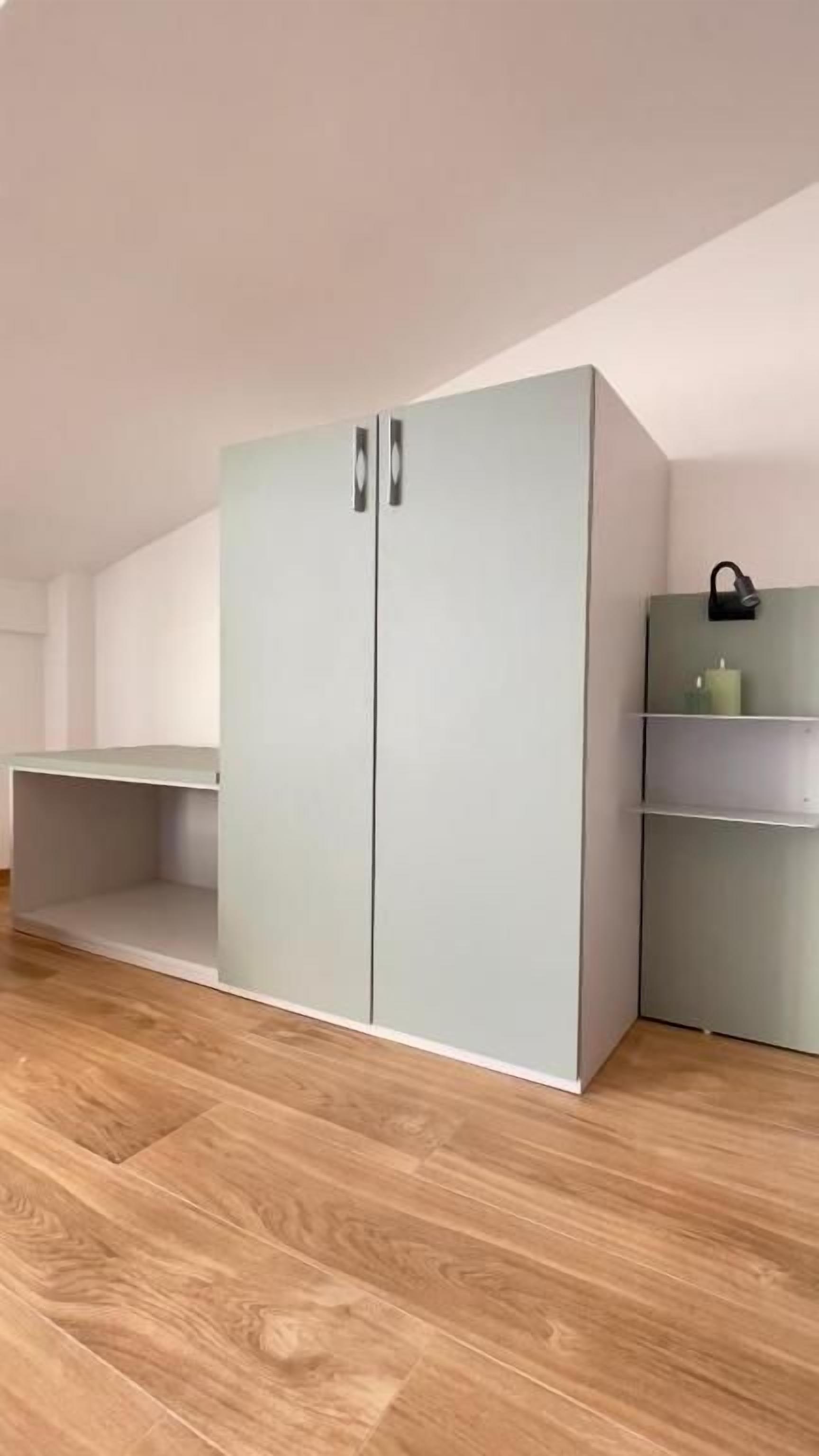 A room with a large wardrobe, a small table, and a shelf unit.