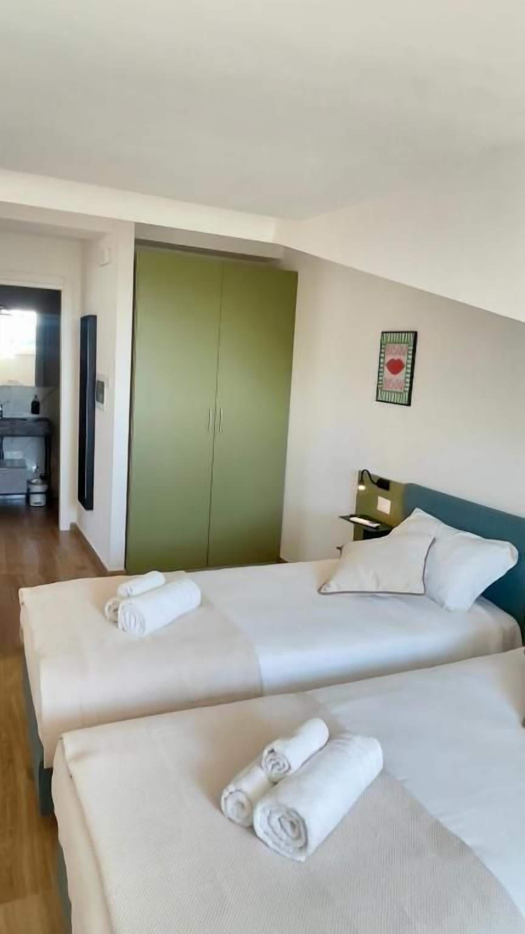 A hotel room with two beds, a green wardrobe, and a small desk.