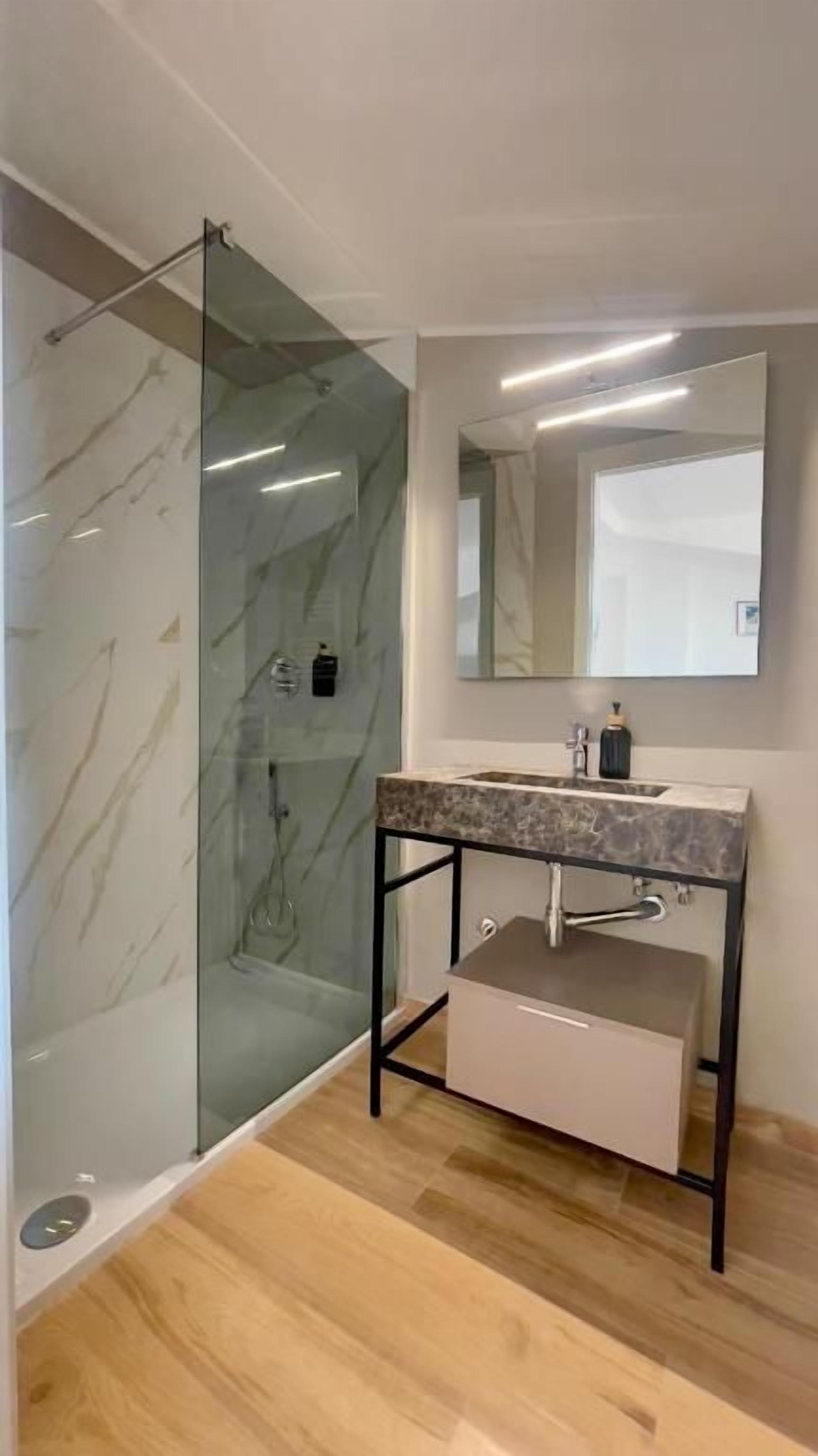 Un bagno moderno con doccia vetrata, lavabo in marmo e uno specchio grande.