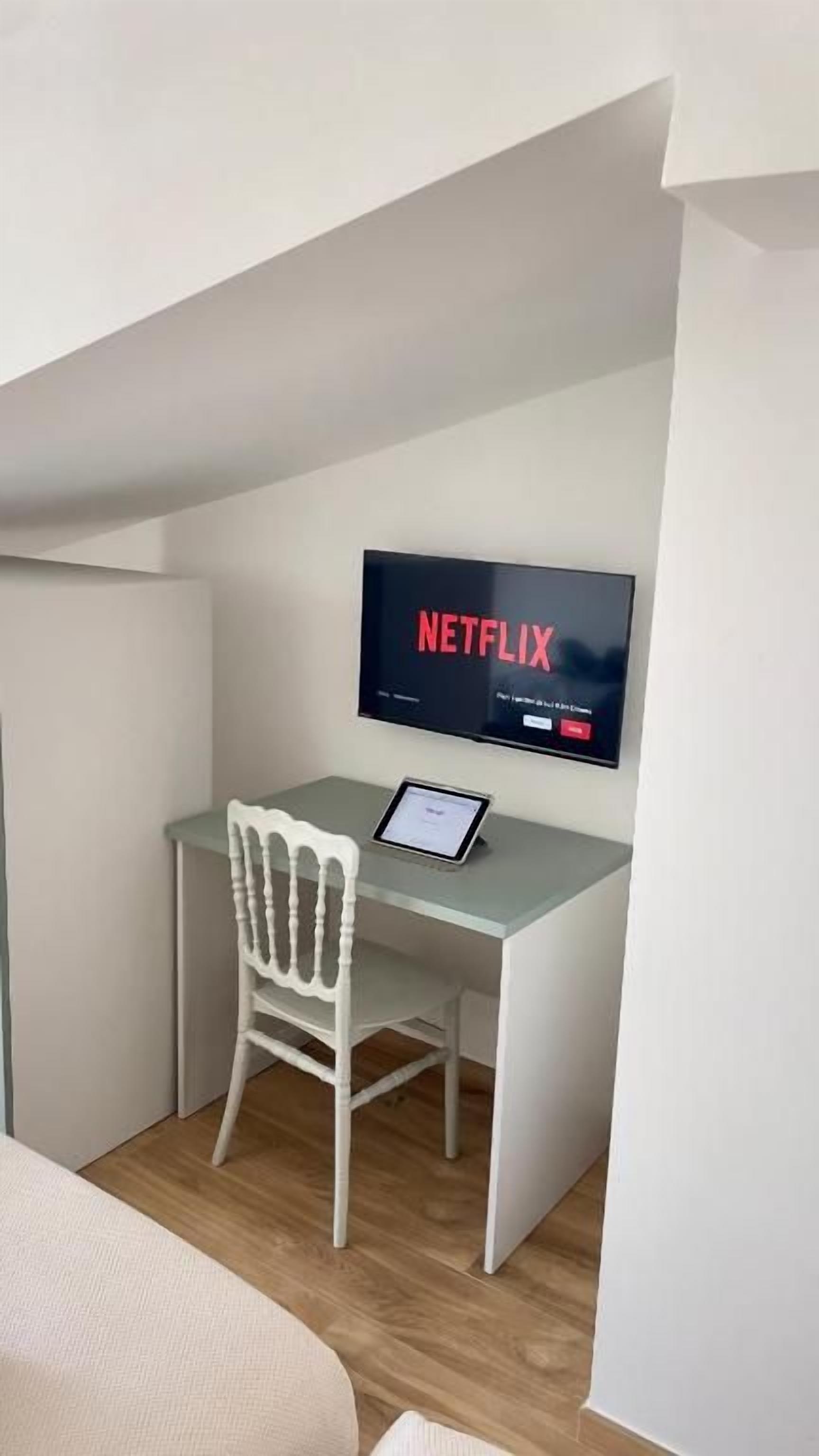 Ein kleiner, moderner Raum mit Schreibtisch, Stuhl und einem Fernseher mit Netflix-Logo.