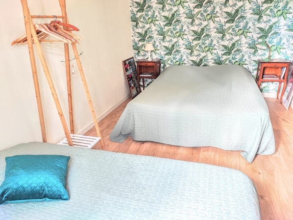 Un dormitorio con dos camas, una escalera de madera, una estantería y un papel tapiz tropical.